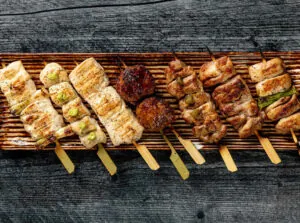 Skewers of grilled meat and vegetables arranged in a row on a wooden platter, set on a rustic gray wooden surface.