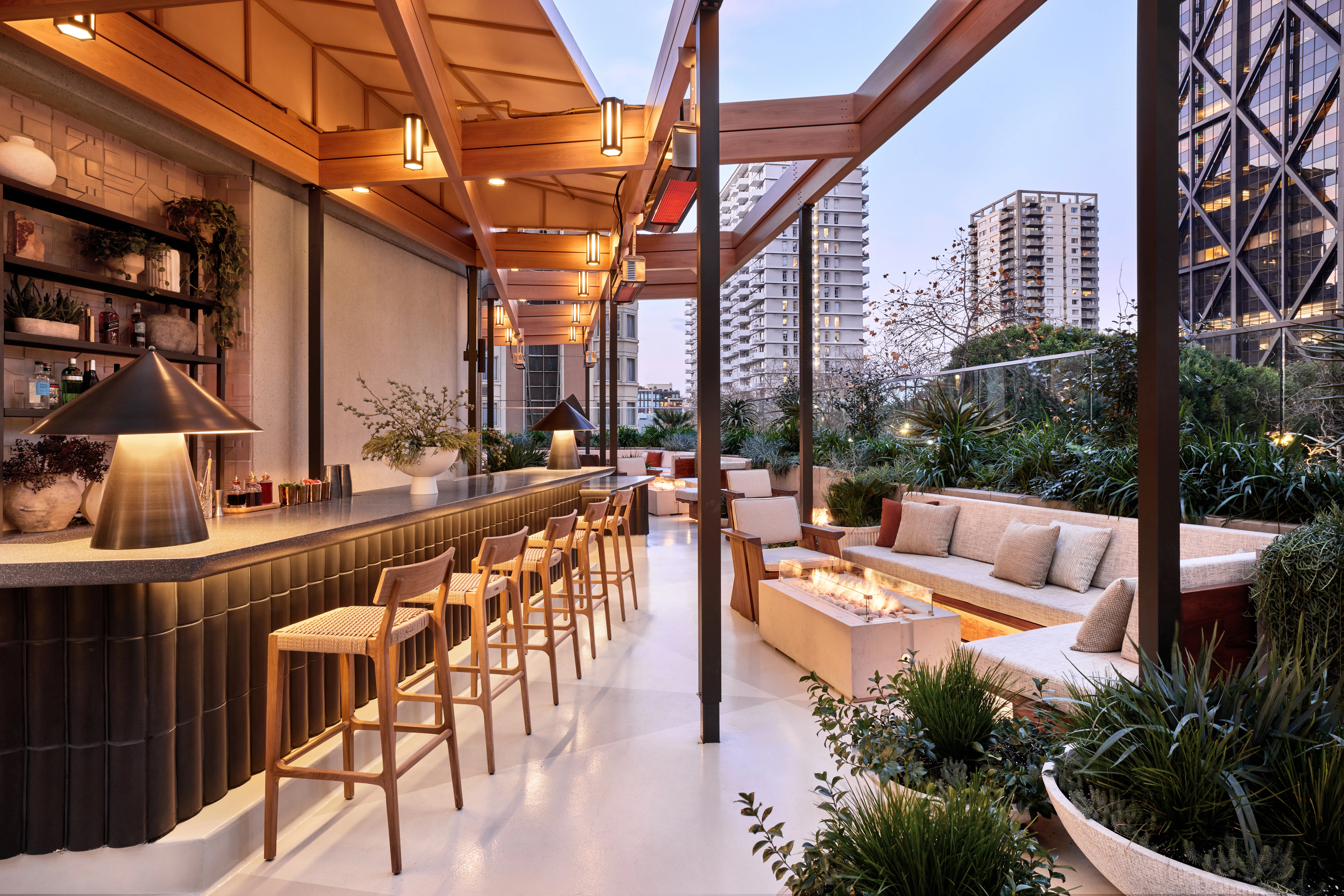 Outdoor terrace bar at The Jay Hotel featuring a sleek bar with wooden stools, comfortable lounge seating, and a cozy fire pit.